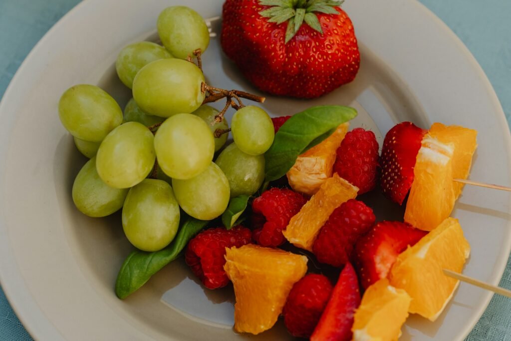 Cachorro pode comer morango: morango vermelho ao lado de um cacho de uvas verdes em um prato, ilustrando a diferença entre as duas frutas