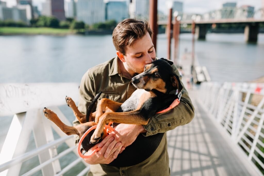 Como o cachorro diz eu te amo - tutor em pé abraçando o cachorro ao ar livre, vínculo afetivo