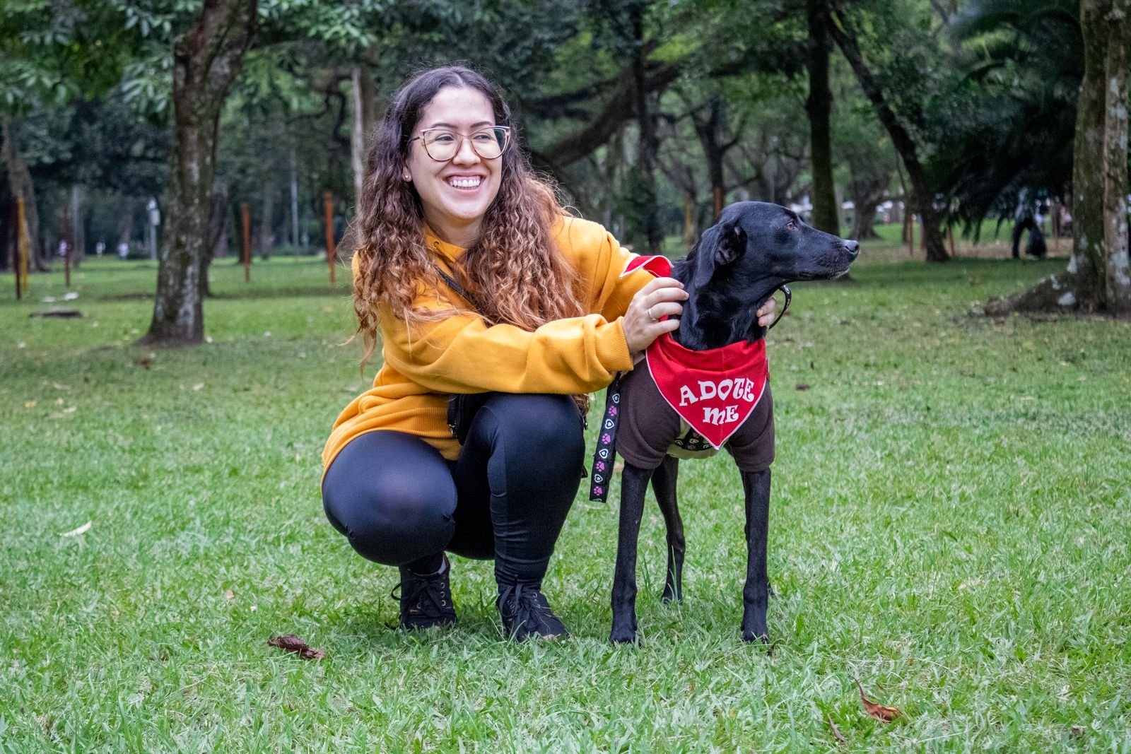 Benefícios de ter um cachorro em casa: mulher sorridente com cachorro resgatado usando bandana escrito adote-me