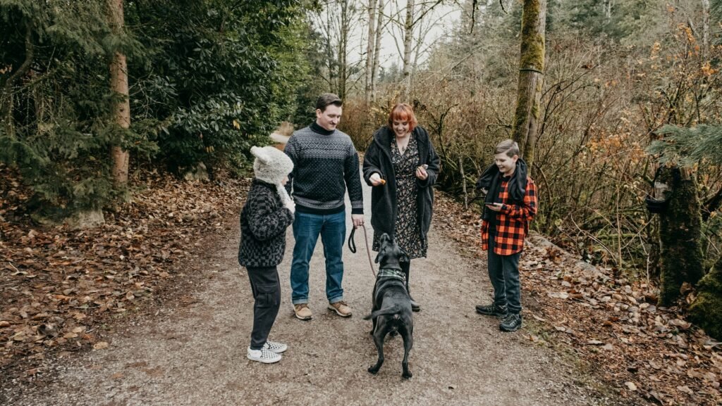 Benefícios de ter um cachorro em casa: família com duas crianças caminhando com o cão em trilha na floresta