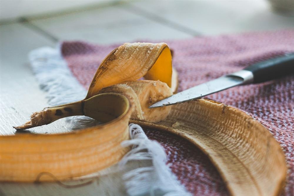Cachorro pode comer banana? O que saber antes de oferecer essa fruta ao seu cão Cachorro pode comer banana: banana descascada sendo cortada com faca sobre um pano de cozinha