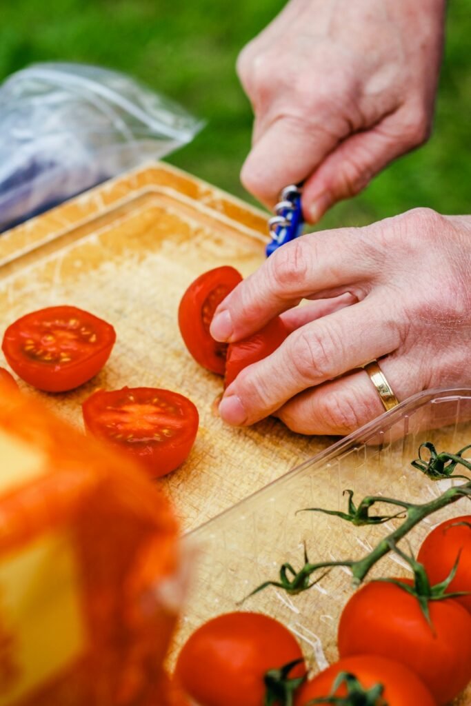 Cachorro pode comer tomate: mãos cortando tomates maduros ao meio sobre uma tábua de madeira