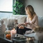 Como treinar cão de serviço em casa: tutora sentada no sofá da sala oferecendo petisco para um cão branco durante sessão de treino doméstico