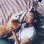 Dormir com o cachorro faz mal espiritualmente: mulher deitada em cama com cachorro shiba inu, vista de cima, ambiente aconchegante