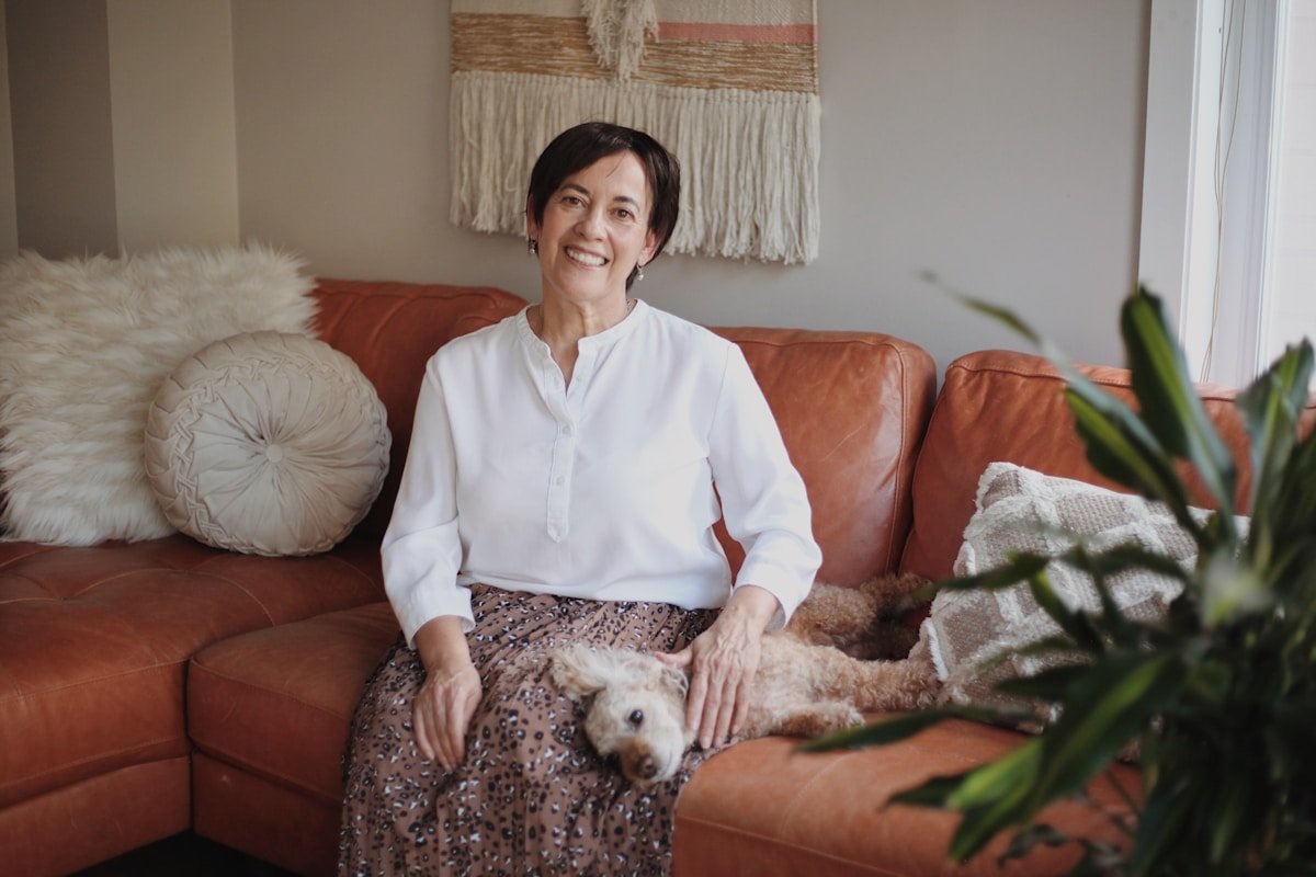 Vermes de Cachorro: Guia Completo para Tutores Prevenirem e Tratarem Tutora sorridente sentada no sofa com seu cachorro no colo, representando o acompanhamento da saude do pet