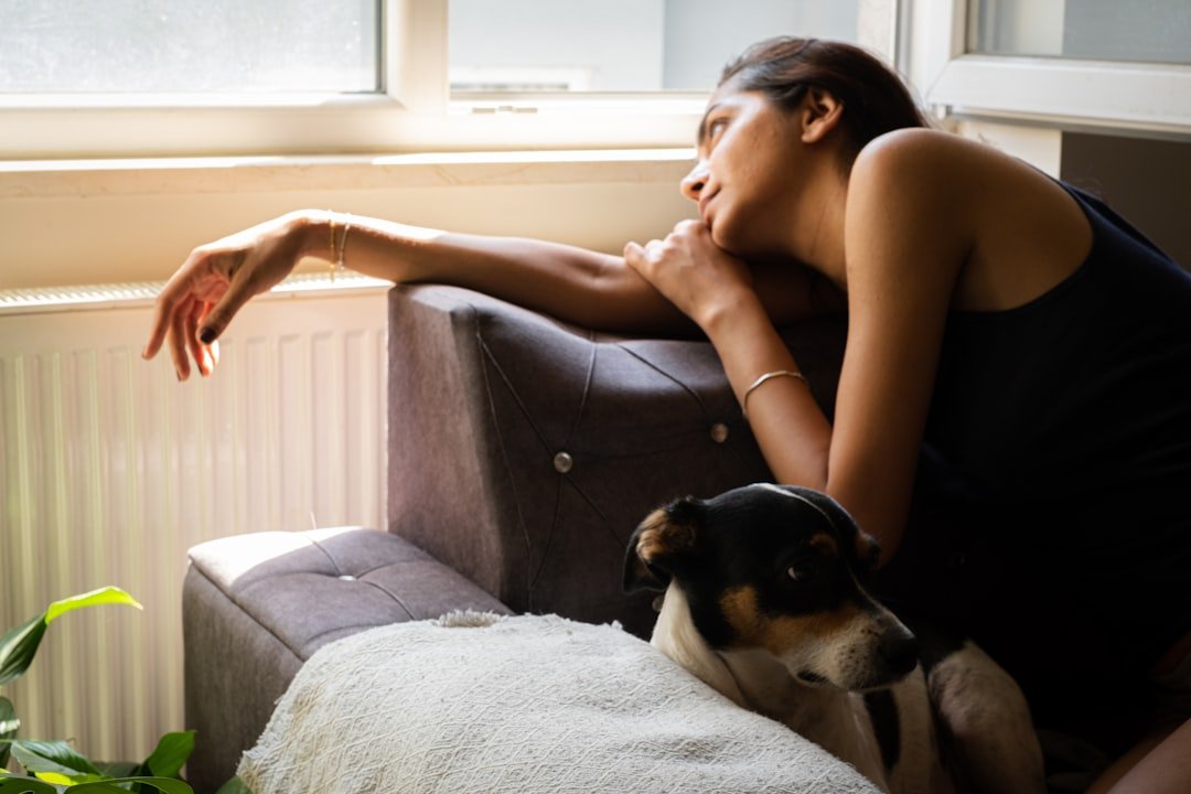 Pessoas que atraem cachorros espiritualmente: mulher em silêncio junto à janela com cachorro encostado tranquilamente ao seu lado
