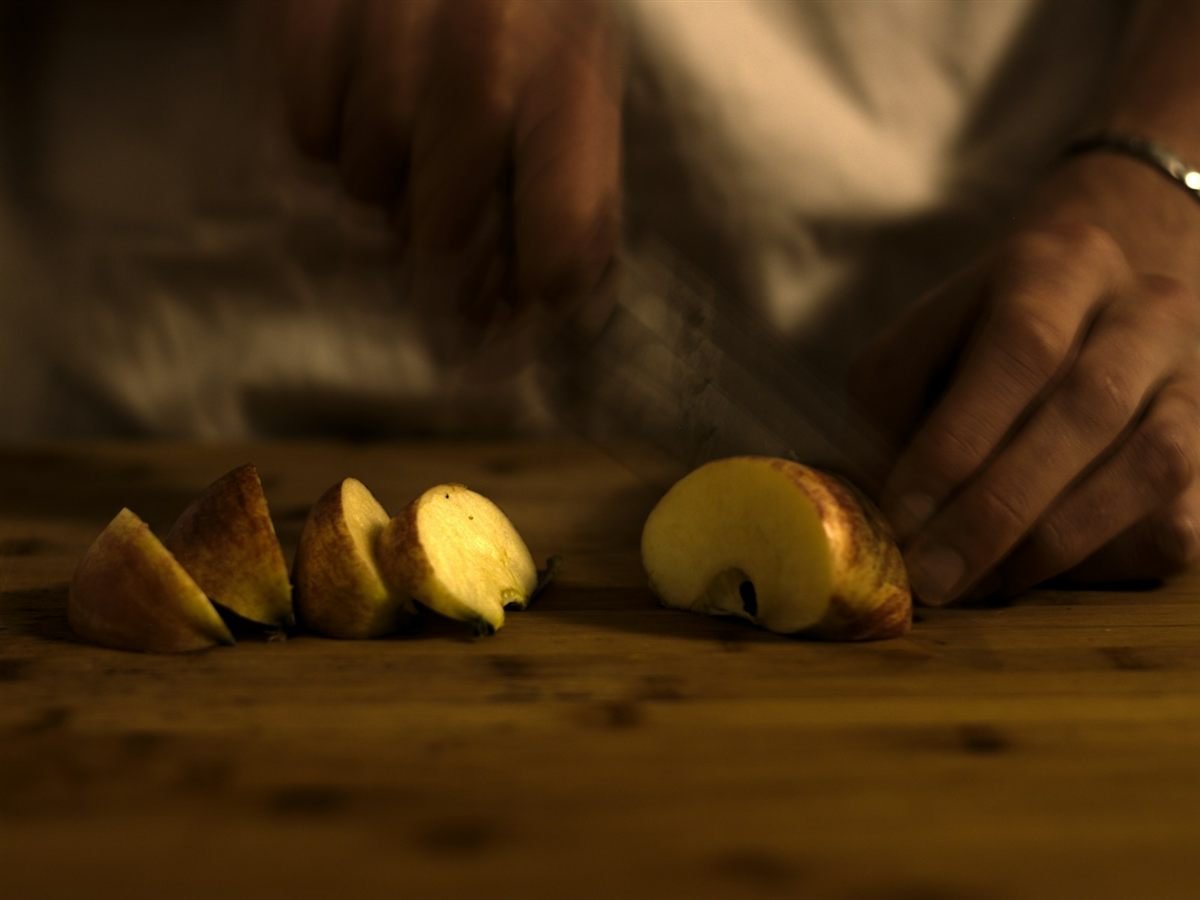 Mãos cortando uma maçã em fatias sobre uma tábua