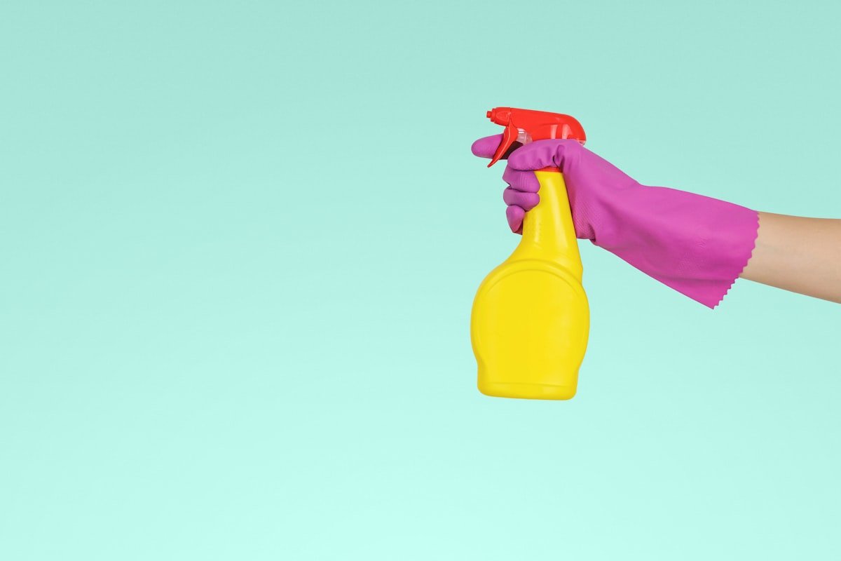 Convulsão em cachorro: mão com luva de borracha rosa segurando um frasco spray amarelo de produto de limpeza