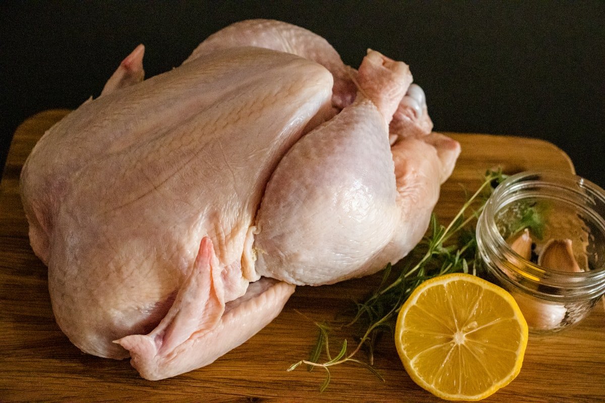 Nutrientes essenciais para cães: frango cru inteiro sobre tábua de madeira, ao lado de ervas e limão
