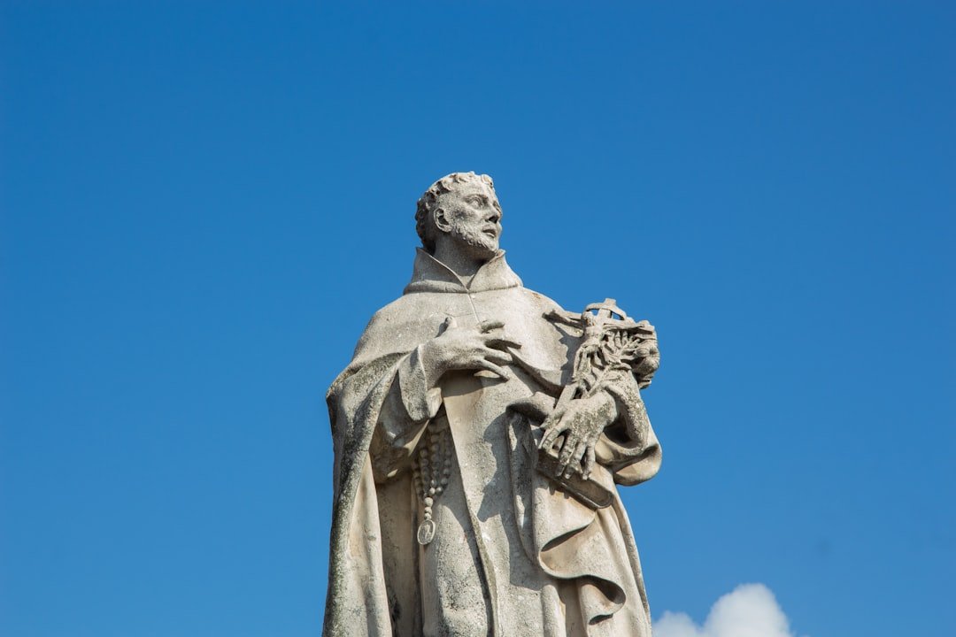 Oração de proteção para o cachorro: estátua de frade franciscano segurando um crucifixo contra o céu azul