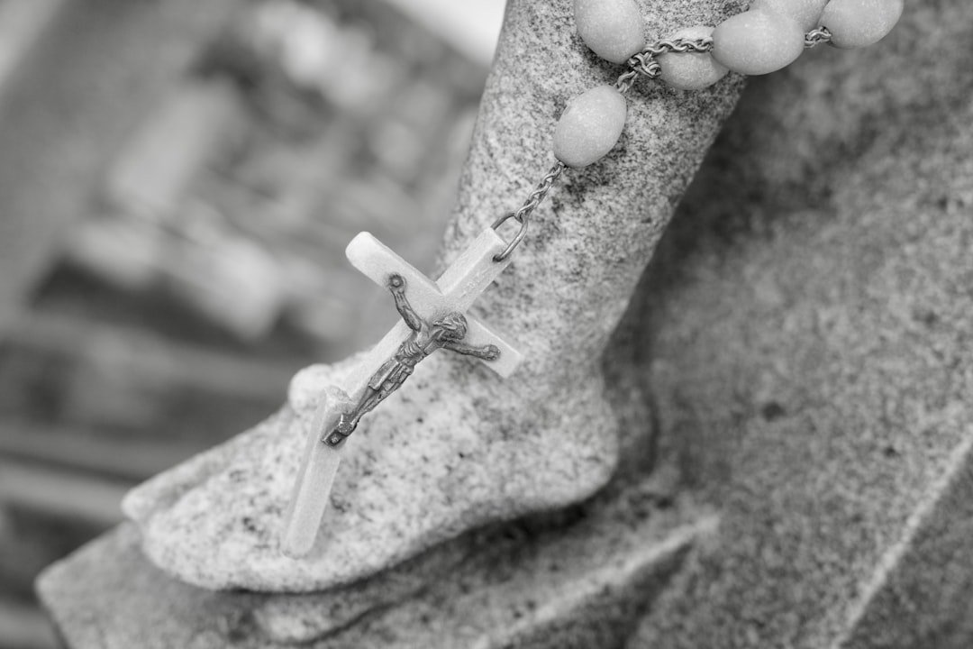 Oração de proteção para o cachorro: terço com crucifixo apoiado sobre o pé de uma estátua de pedra