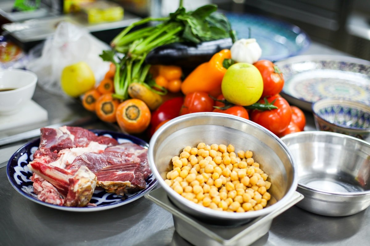 Proteínas para cachorros: pedaço de carne crua com osso ao lado de uma tigela de grão-de-bico e vegetais frescos